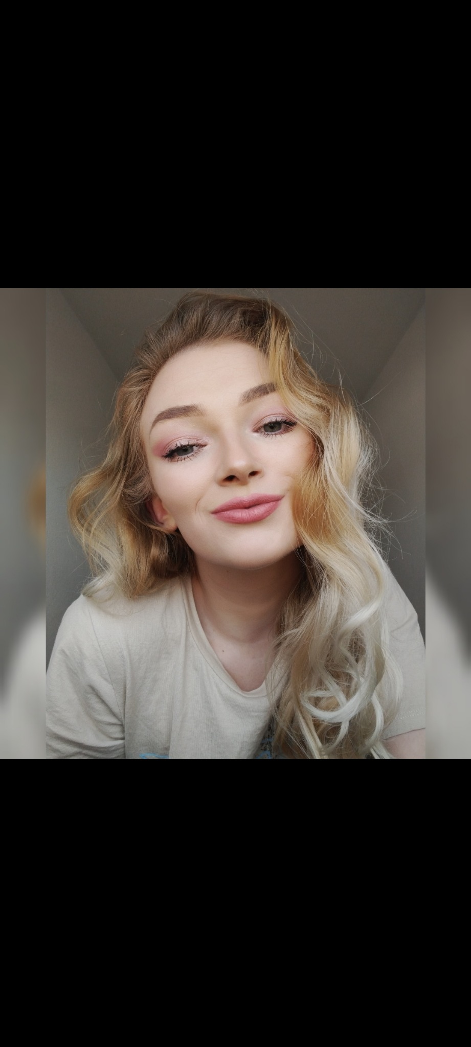 Portret uśmiechniętej blondynki z delikatnym, różowym makijażem oczu i ust, sfotografowanej w naturalnym świetle.