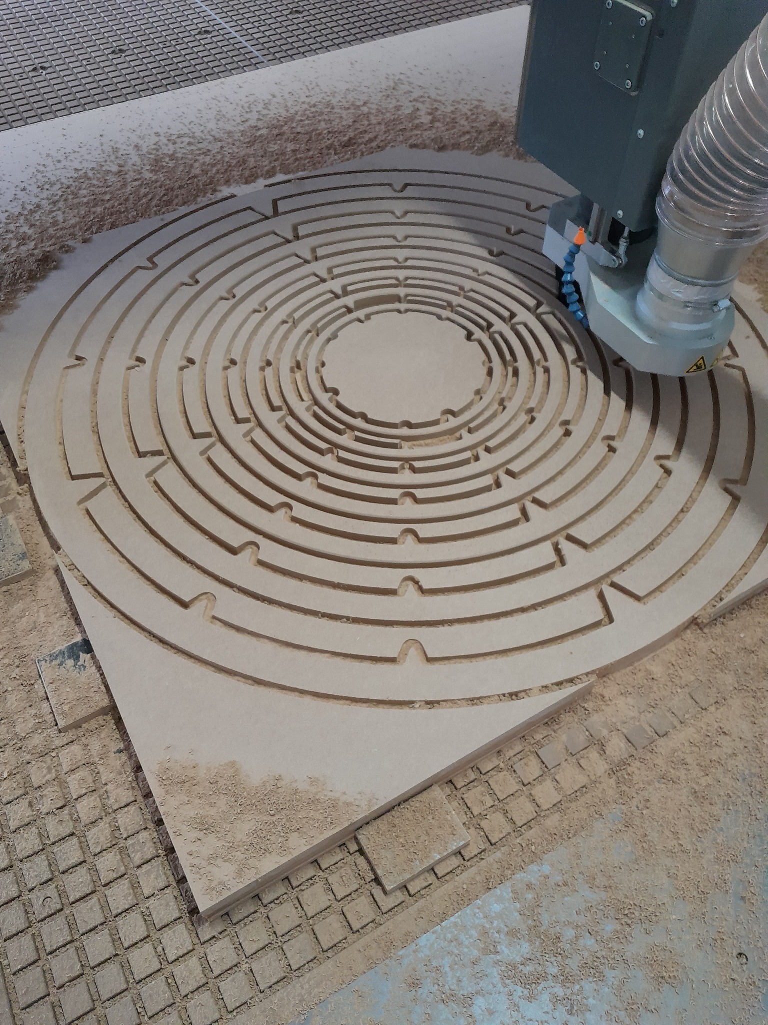 Frezarka CNC wycina okrągły labirynt w płycie MDF, widoczne wióry i system chłodzenia.