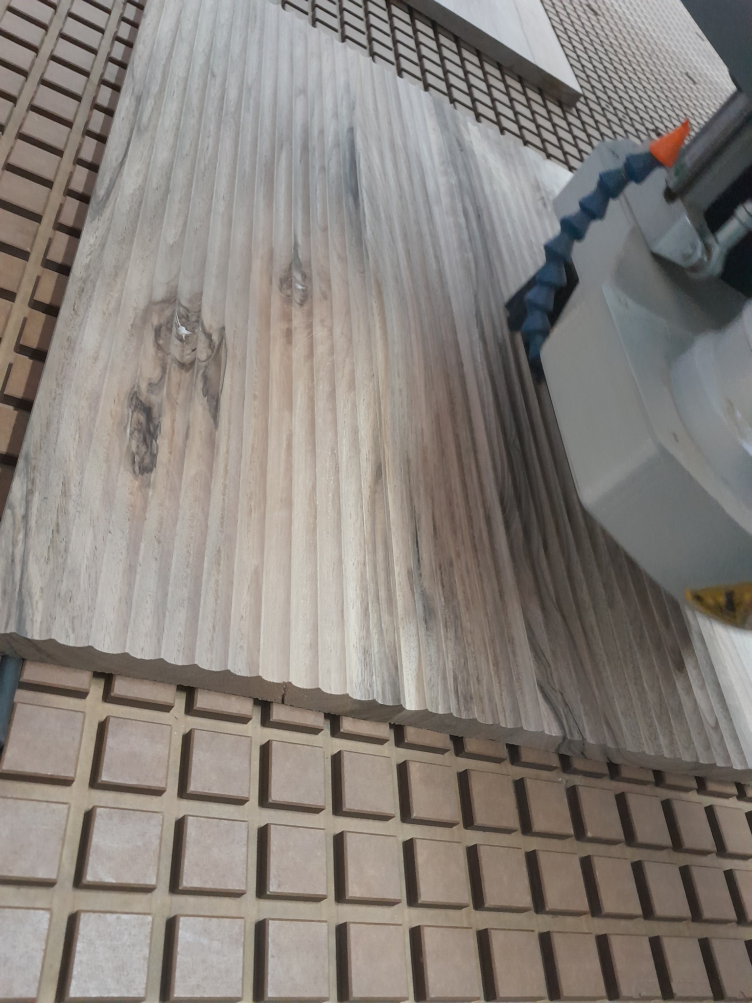 Obróbka CNC drewna z widocznym frezem i rowkowaną powierzchnią, mocowanego na płycie z kwadratowymi elementami