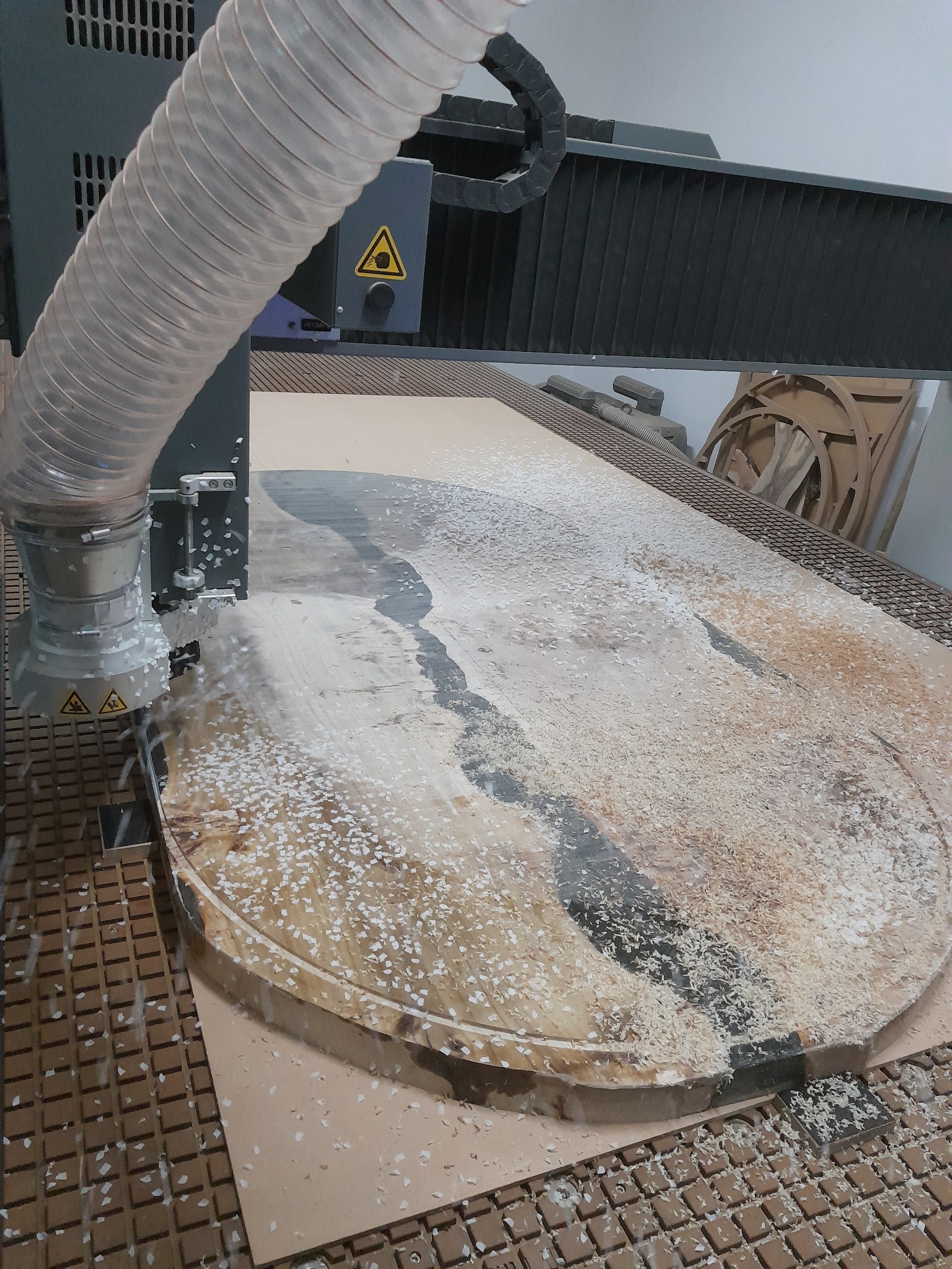 Frezowanie blatu stołu z żywicą epoksydową przy użyciu maszyny CNC, widoczne wióry i system odsysania.