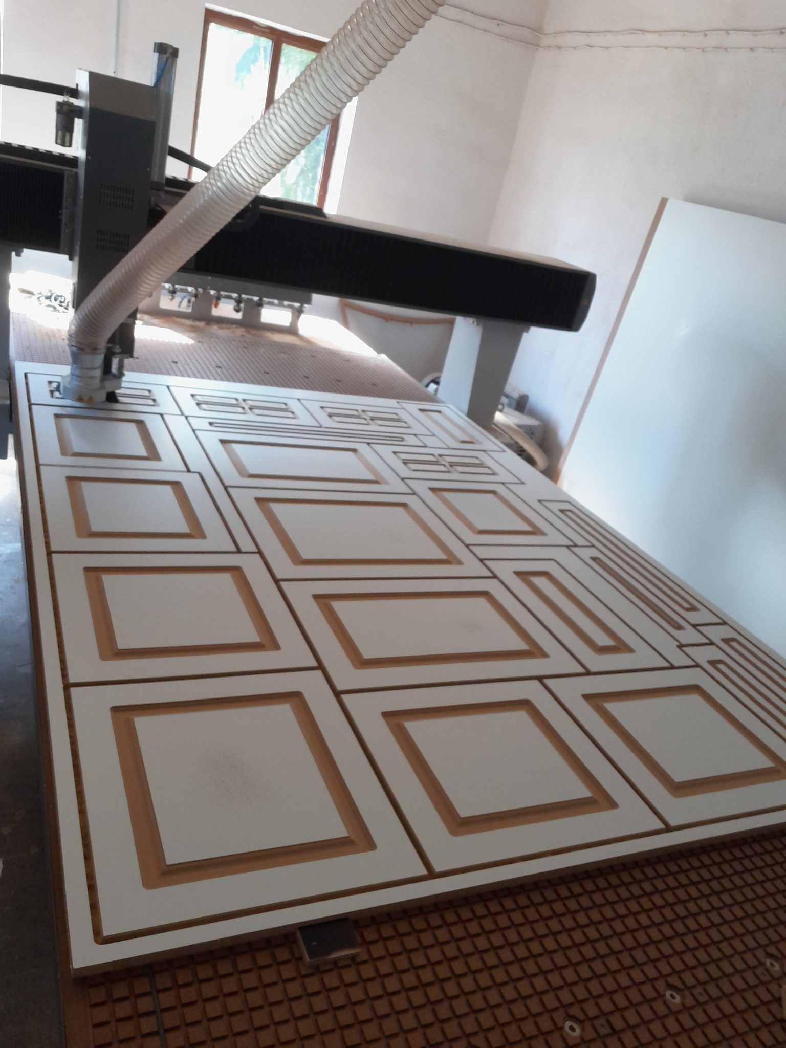 Frezowanie wzoru w płycie MDF na stole frezarki CNC, widoczny przewód odciągu wiórów.