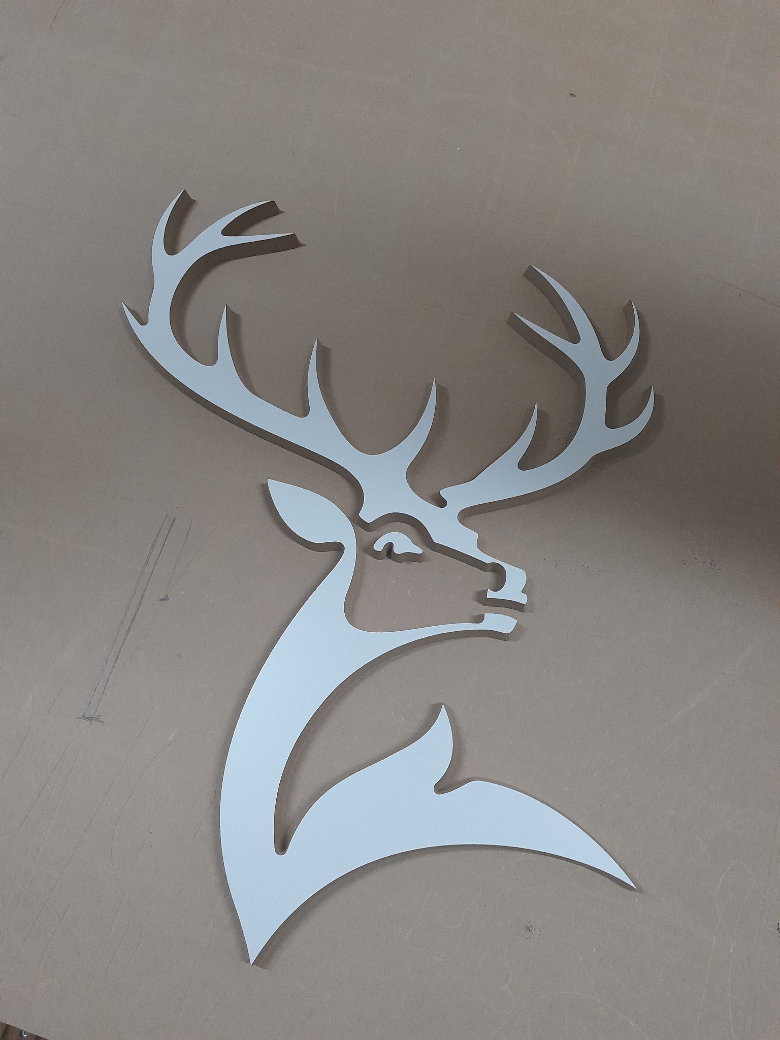 Wycięty z metalu biały profil głowy jelenia z rogami na brązowym tle.