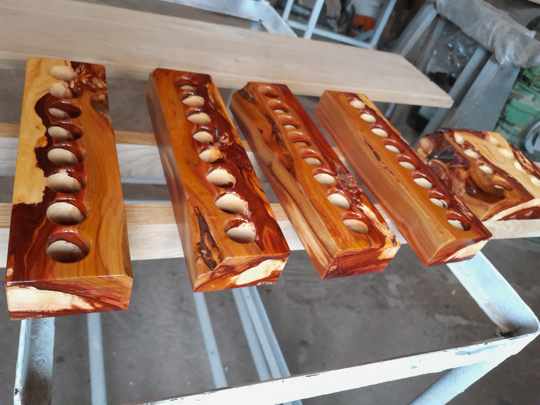 Drewniane, lakierowane bloki z rzędami wywierconych otworów, ukazujące unikalny wzór słojów drewna, leżące na metalowym regale.