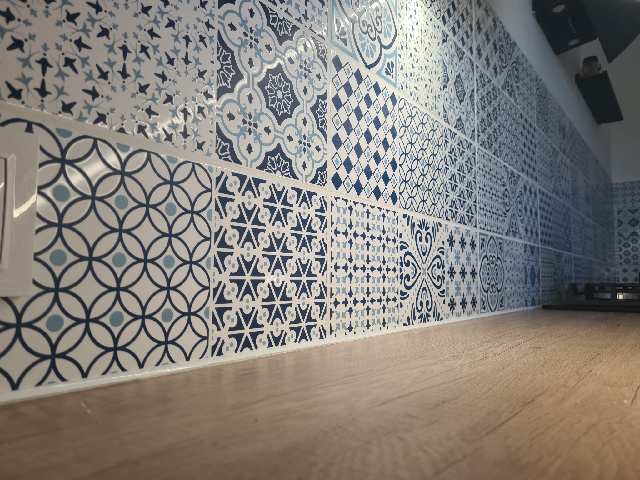 Dekoracyjne, niebiesko-białe płytki ceramiczne z różnymi wzorami na ścianie nad drewnianym blatem kuchennym, widok z niskiej perspektywy.