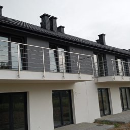 FHU SPAW Smoszna Janusz - Nowoczesne balkony szeregowca z prostymi, metalowymi barierkami, widok z zewnątrz na szary budynek z czarnym dachem.