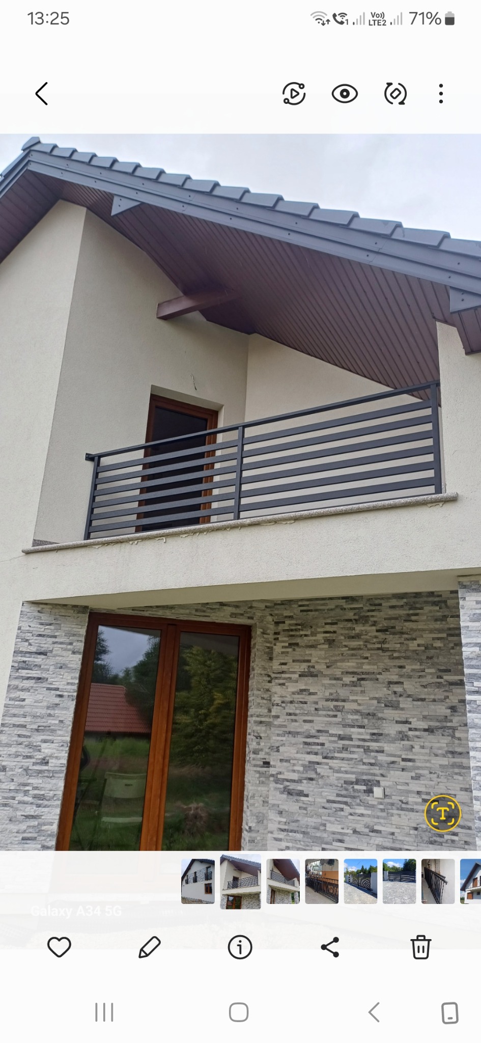 Nowoczesny balkon z poziomą, czarną, metalową konstrukcją zabezpieczającą, widok na dwukondygnacyjny budynek z oknami w drewnianych ramach i elewacją z dekoracyjnego kamienia.