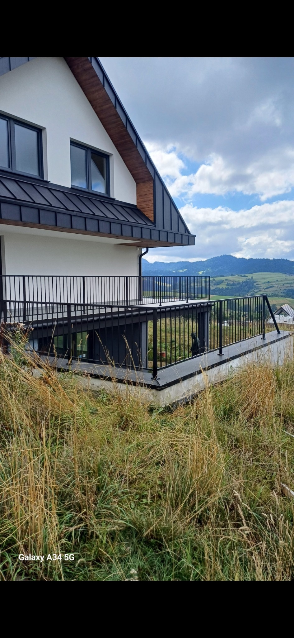 Czarna, nowoczesna balustrada balkonowa z widokiem na górzysty krajobraz, perspektywa z poziomu wysokiej trawy.