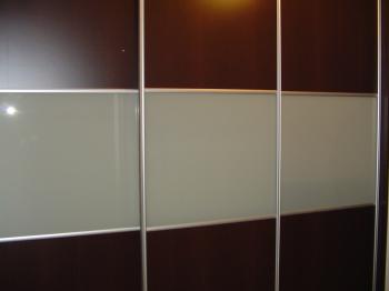 Trzydrzwiowa szafa przesuwna z ciemnobrązowymi panelami i mlecznymi szybami, obramowana srebrnymi profilami.