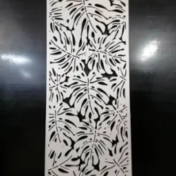 Biały, ażurowy panel dekoracyjny z motywem liści monstery na ciemnym tle, stojący na podłodze.