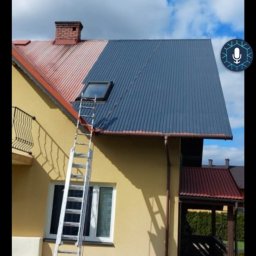 KarMal - Dwukolorowy dach z blachy trapezowej, część pomalowana na szaro, część w kolorze ceglastym, drabina oparta o dach, fragment elewacji domu w kolorze żółtym, sterta drewna na trawniku.