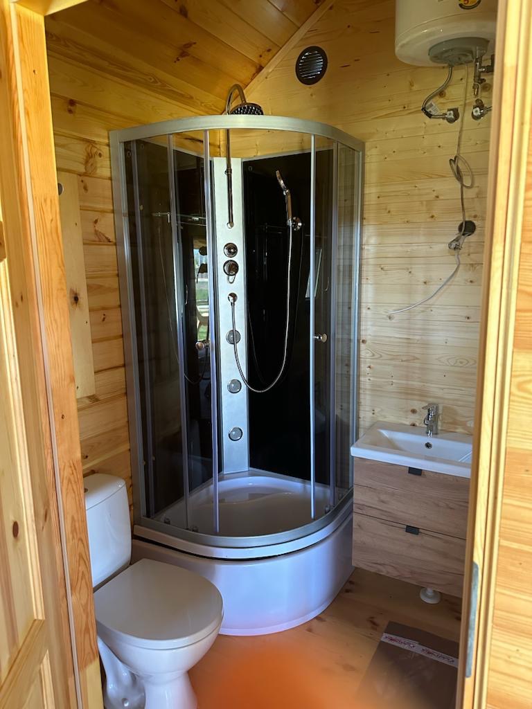 Drewniana łazienka z kabiną prysznicową z hydromasażem, umywalką z szafką w kolorze drewna i toaletą.