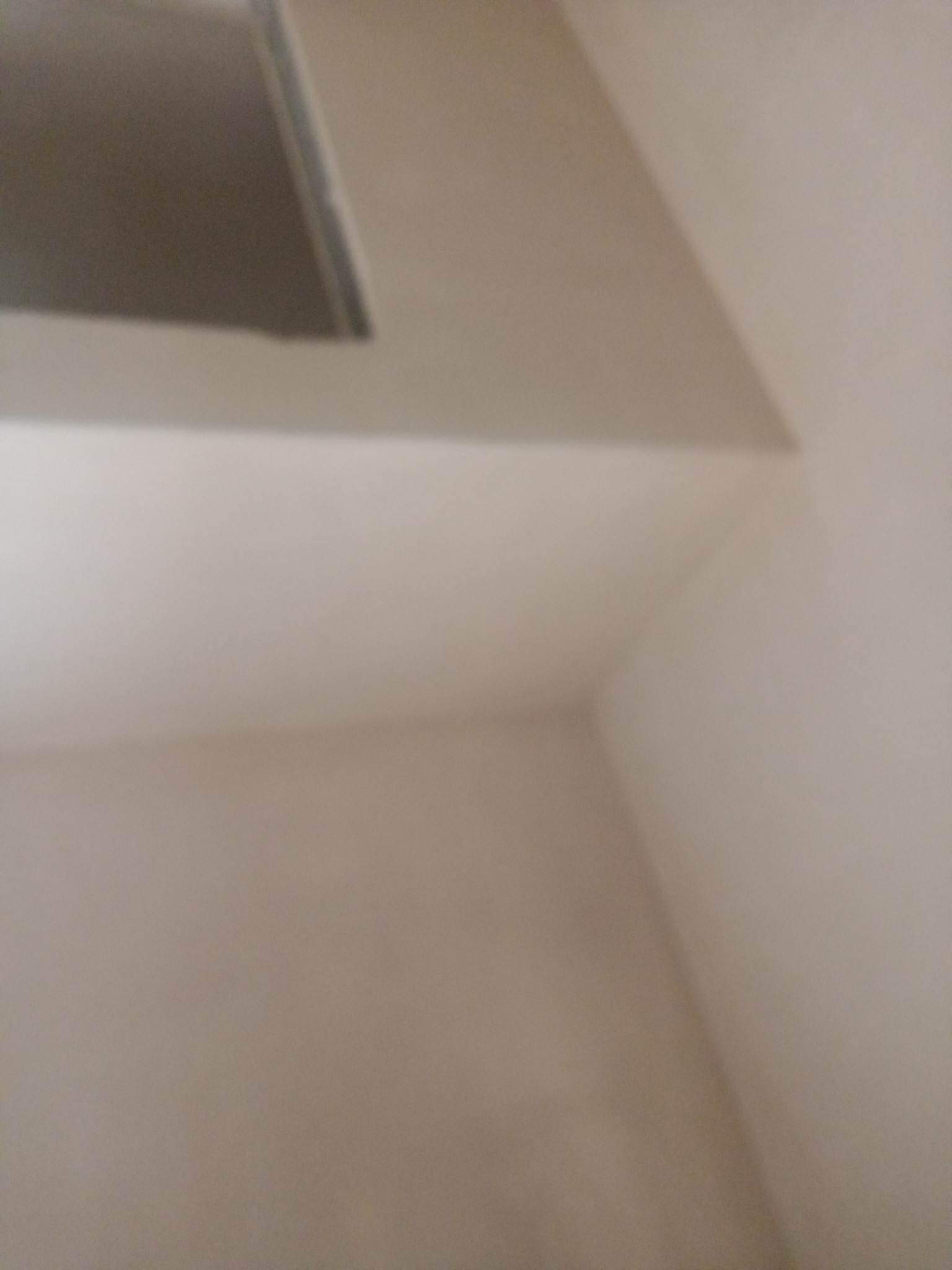 Fragment świeżo otynkowanego, gładkiego sufitu i ściany w jasnym odcieniu, widoczny pod kątem.