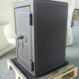 Brązowy sejf obity skórą z elektronicznym zamkiem, ozdobne przeszycia na krawędziach, umieszczony na drewnianej palecie.