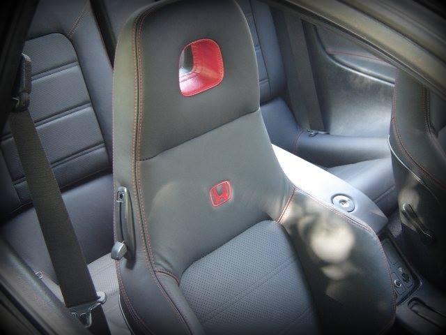 Szare skórzane siedzenie samochodowe z czerwonymi akcentami i logo, widoczne przeszycia i perforowana skóra, regulacja oparcia