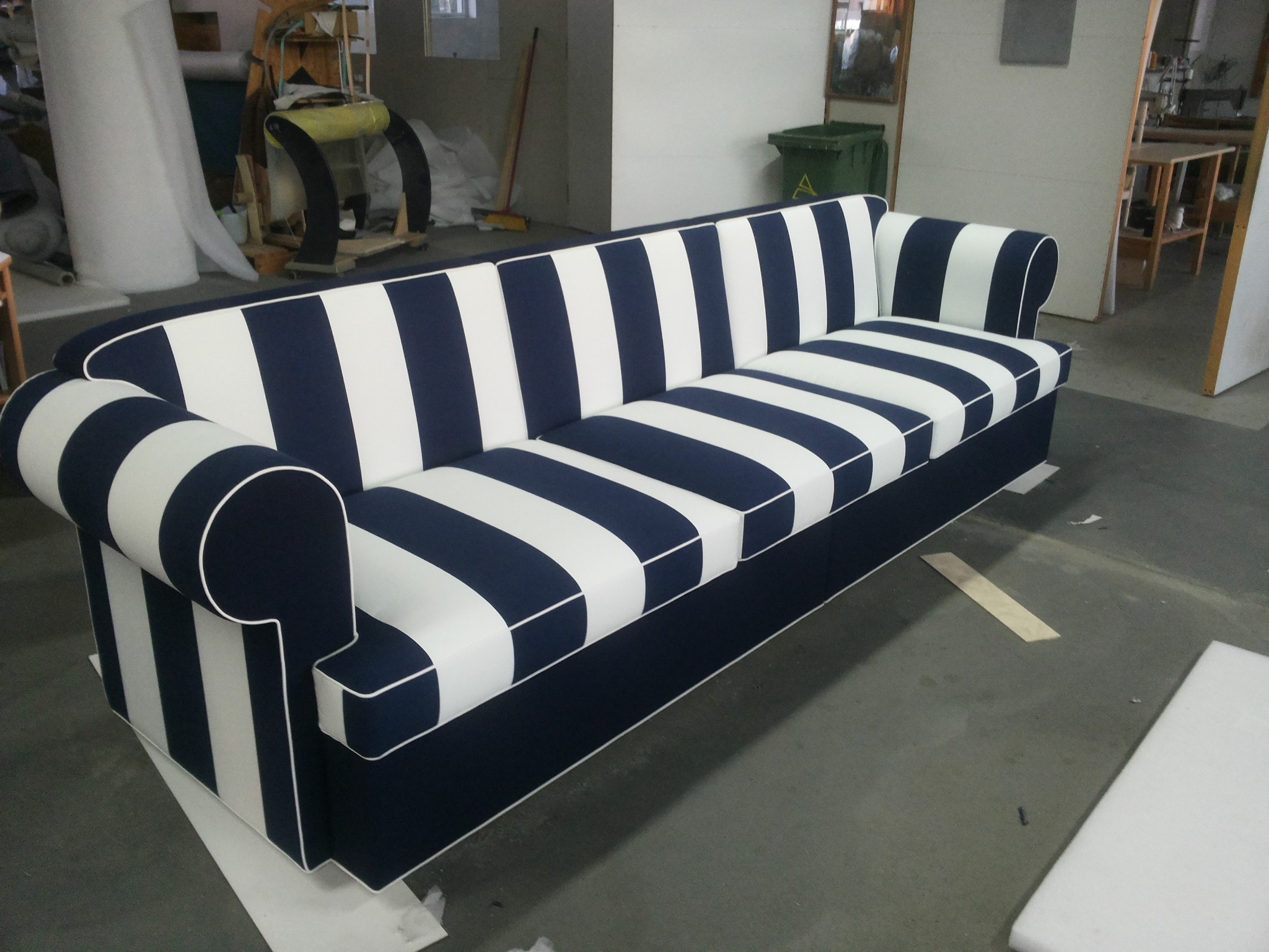 Gotowa sofa w biało-granatowe pasy w warsztacie w Banino, widoczne materiały i narzędzia w tle.