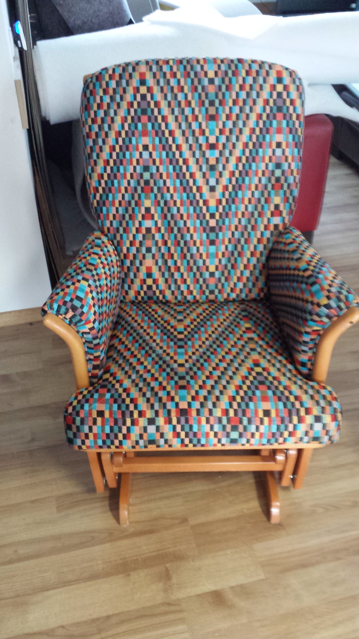 Fotel bujany po renowacji z nową, wzorzystą tapicerką w odcieniach czerwieni, błękitu i czerni, drewniane podłokietniki i podstawa.