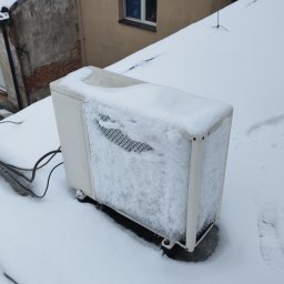 SYSTEMUS SP. Z O. O. - Zewnętrzna jednostka klimatyzacji na dachu budynku, częściowo zasypana śniegiem, z widoczną kratką wlotową i kablami zasilającymi.