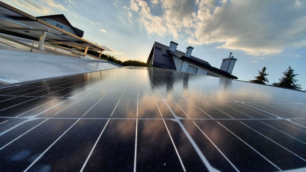 Instalacja paneli słonecznych w Zbylitowskiej Górze, z widocznym odbiciem nieba i chmur na powierzchni paneli, zamontowanych na dachu budynku.