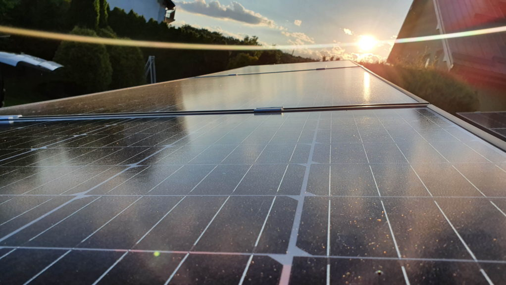 Panel słoneczny z widocznymi zabrudzeniami na powierzchni, zamontowany na dachu domu w promieniach zachodzącego słońca.