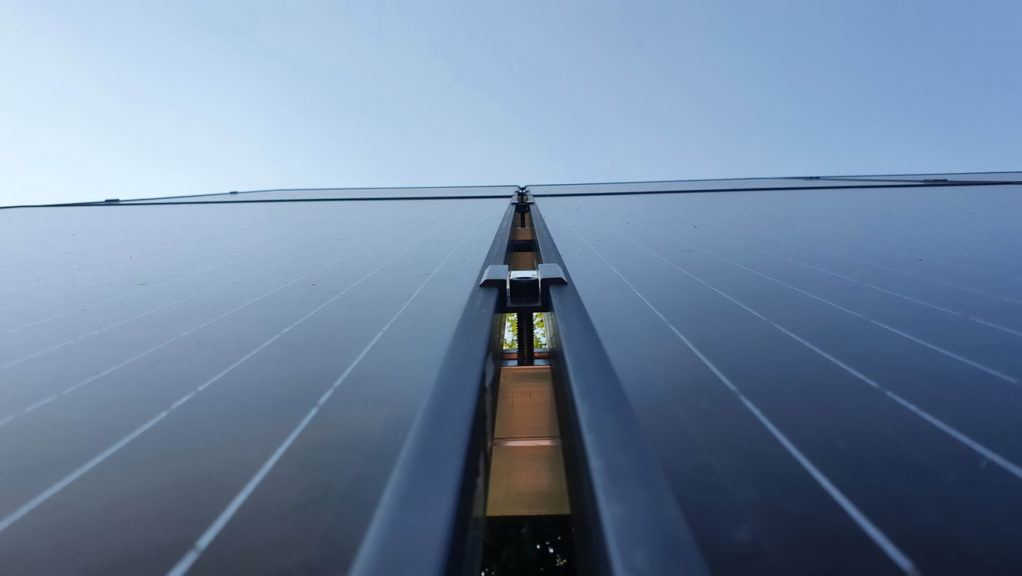 Widok z dołu na zainstalowane panele słoneczne, widoczne mocowania i przestrzeń między panelami, niebo w tle.