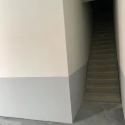 Klatka schodowa w Głogowie po malowaniu ścian na biało i szaro, widoczne schody z żółtymi pasami antypoślizgowymi.