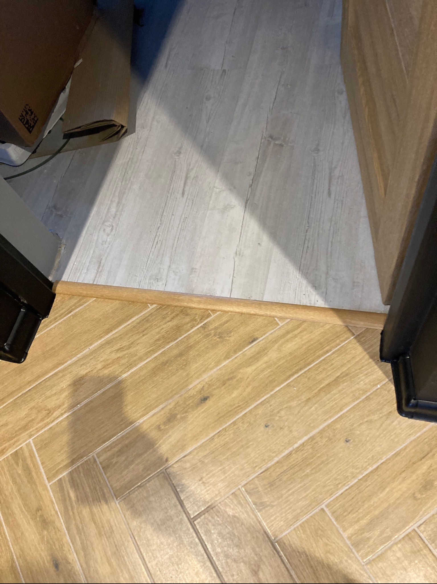 Połączenie dwóch rodzajów podłóg: jasnych paneli imitujących drewno i brązowych płytek ułożonych w jodełkę, oddzielonych drewnianą listwą przypodłogową.