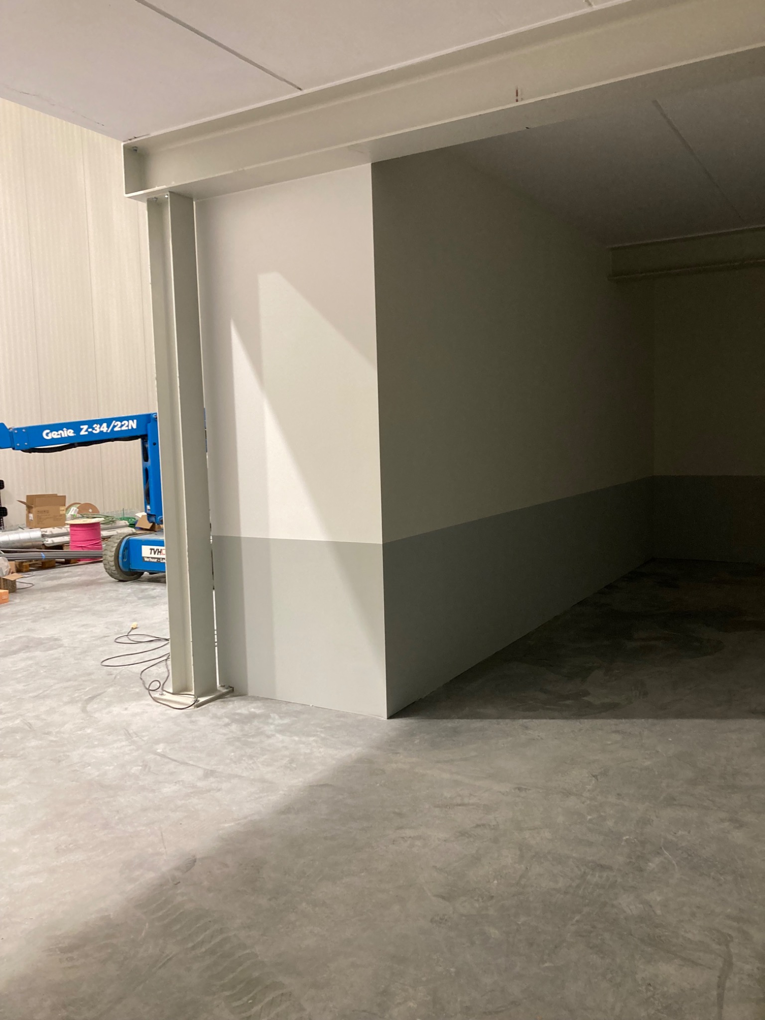 Świeżo pomalowane ściany biura z szarą lamperią, widoczny podnośnik koszowy Genie Z-34/22N w tle.