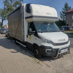 Biały samochód dostawczy Iveco z plandeką, zaparkowany na chodniku w słoneczny dzień, z widoczną tablicą rejestracyjną EL 5HS94 i logiem MIDAR.COM.PL na zabudowie.