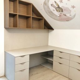 AVAR BESPOKE SPÓŁKA Z OGRANICZONĄ ODPOWIEDZIALNOŚCIĄ - Biało-beżowe biurko narożne z szufladami i półkami, nad nim drewniany regał z przegródkami, na ścianie naklejka z księżycem i królikiem, poddasze.