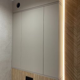 AVAR BESPOKE SPÓŁKA Z OGRANICZONĄ ODPOWIEDZIALNOŚCIĄ - Beżowa szafka wisząca z trzema drzwiczkami, zamontowana w łazience z drewnianą boazerią i oświetleniem LED, widoczny przycisk spłuczki.