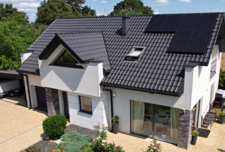 Nowoczesny dom jednorodzinny z szarą dachówką i zamontowanymi panelami słonecznymi na dachu, widok z góry.