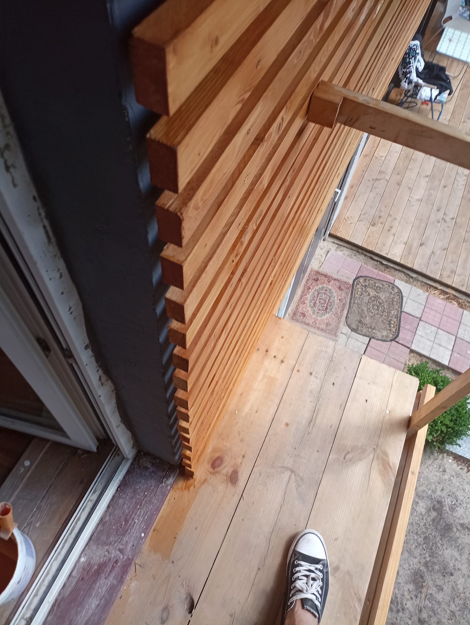 Montaż drewnianej ażurowej ściany na zewnątrz budynku, widoczne surowe drewno, fragment elewacji i podłogi tarasu w trakcie budowy.