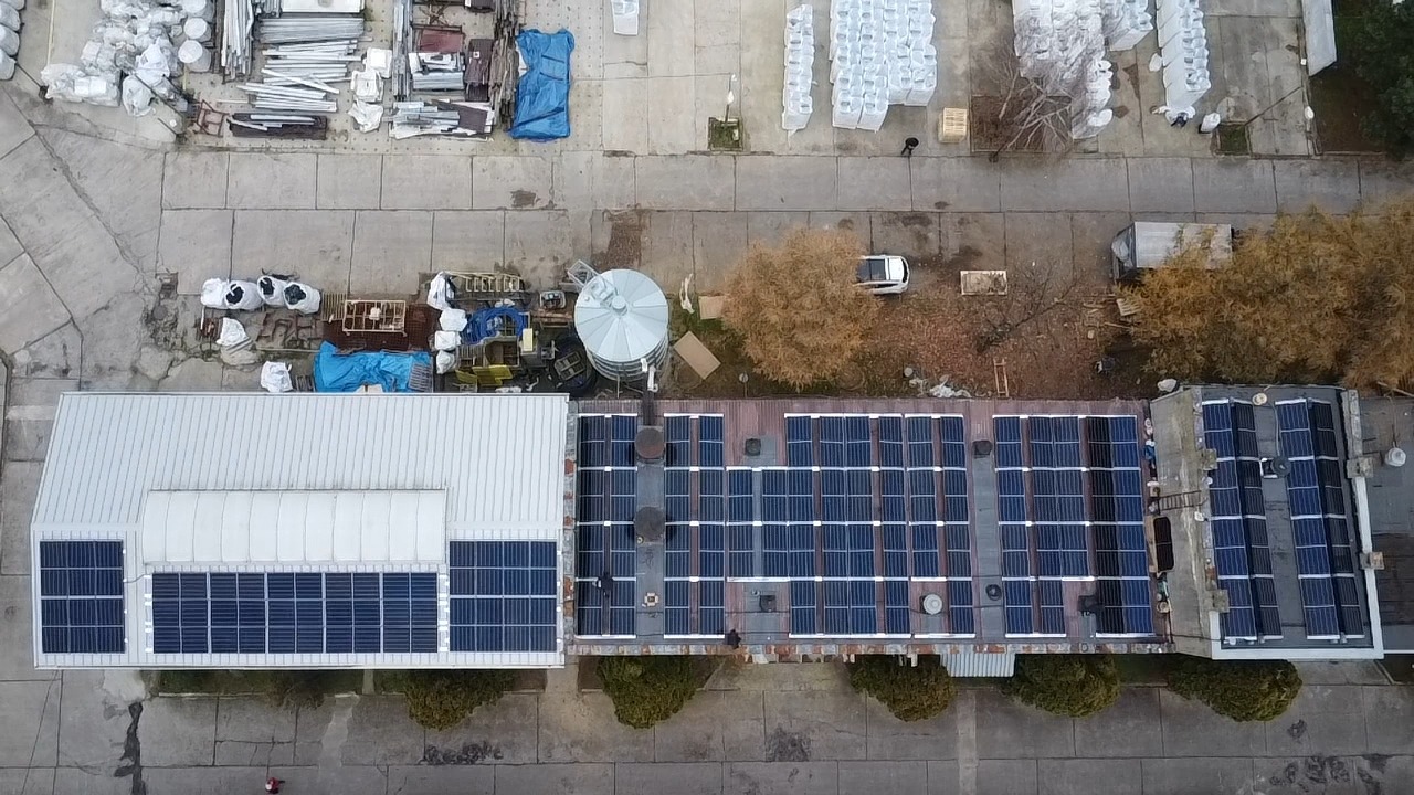 Widok z góry na budynek z panelami słonecznymi na dachu, obok silos i składowane materiały budowlane.