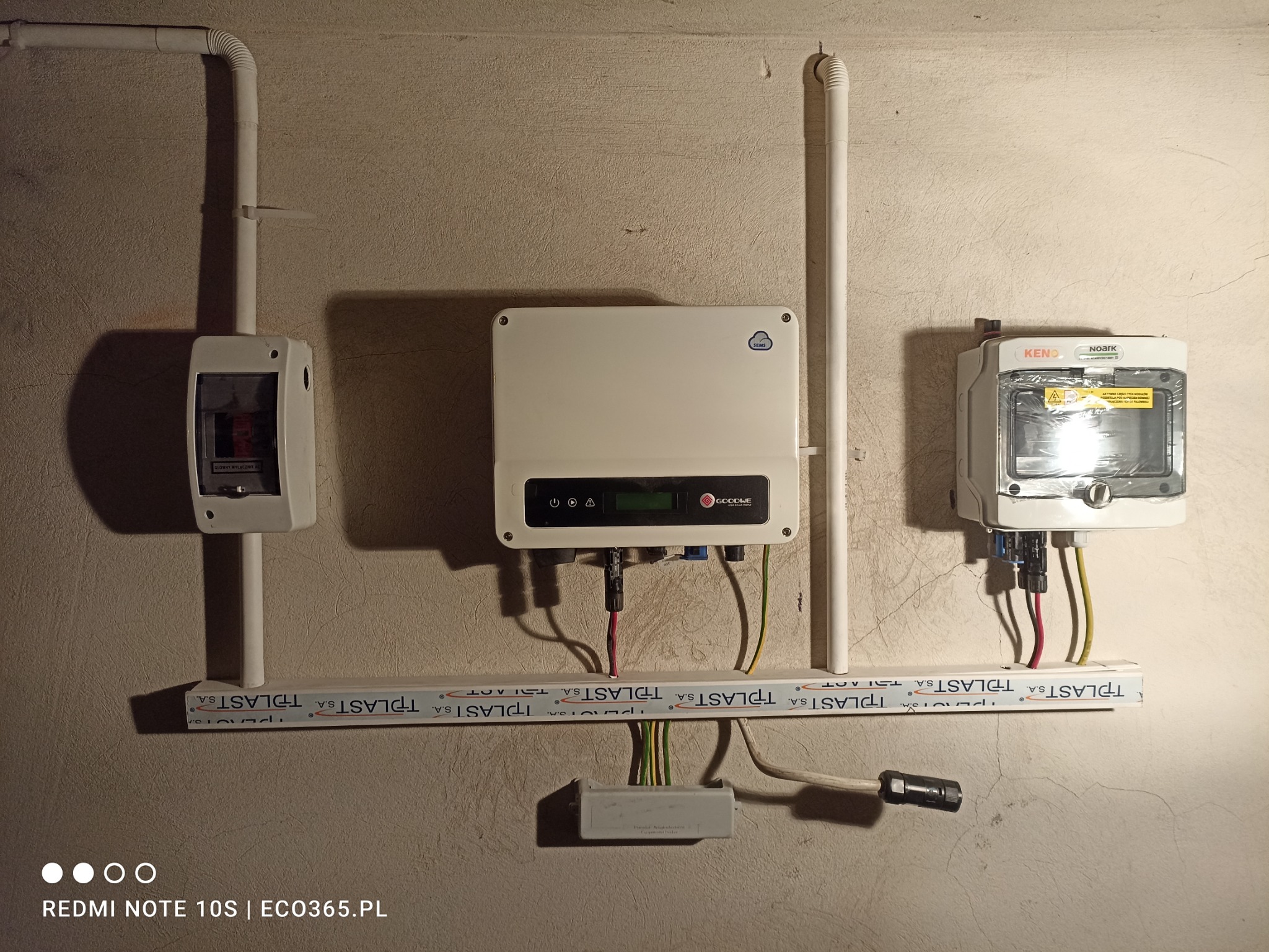 Instalacja elektryczna: Inwerter fotowoltaiczny Goodwe, zabezpieczenia Noark i rozłącznik w obudowach na ścianie z widocznymi przewodami w korytkach TPLAST.