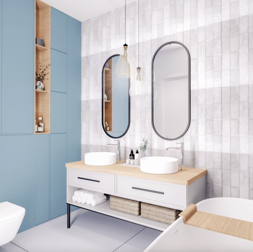 Nowoczesna łazienka z dwoma okrągłymi umywalkami na blacie z jasnego drewna, owalne lustra w czarnych ramach, wiszące lampy z przezroczystego szkła i niebieska zabudowa meblowa z otwartymi półkami.