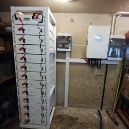 Givemo Michał Misiaszek - Bateria magazynu energii fotowoltaicznej w białej obudowie, z widocznymi przewodami i elementami instalacji, zamontowana w pomieszczeniu z wykończeniem z płytek.