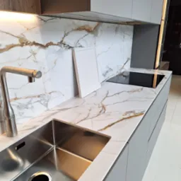 Nowoczesna kuchnia z blatem imitującym marmur, srebrnym zlewem i płytą indukcyjną, uzupełniona o białą ramkę opartą o ścianę.