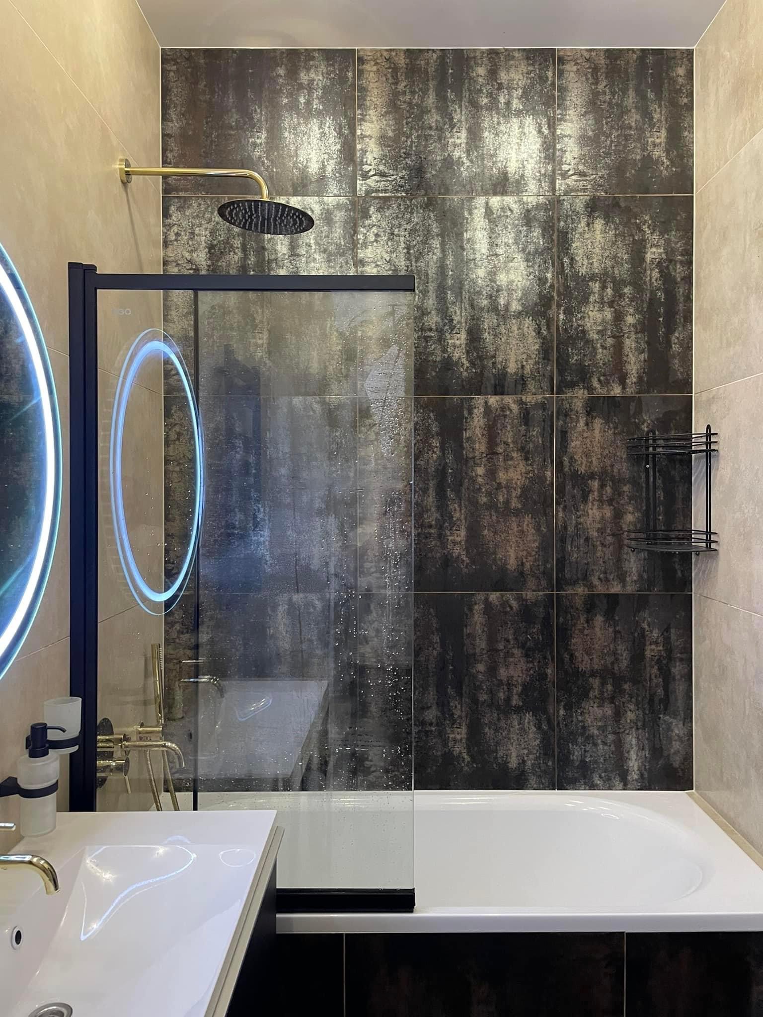 Nowoczesna łazienka z kabiną prysznicową typu walk-in, czarną armaturą, okrągłym lustrem z podświetleniem LED i płytkami imitującymi rdzę na ścianie.