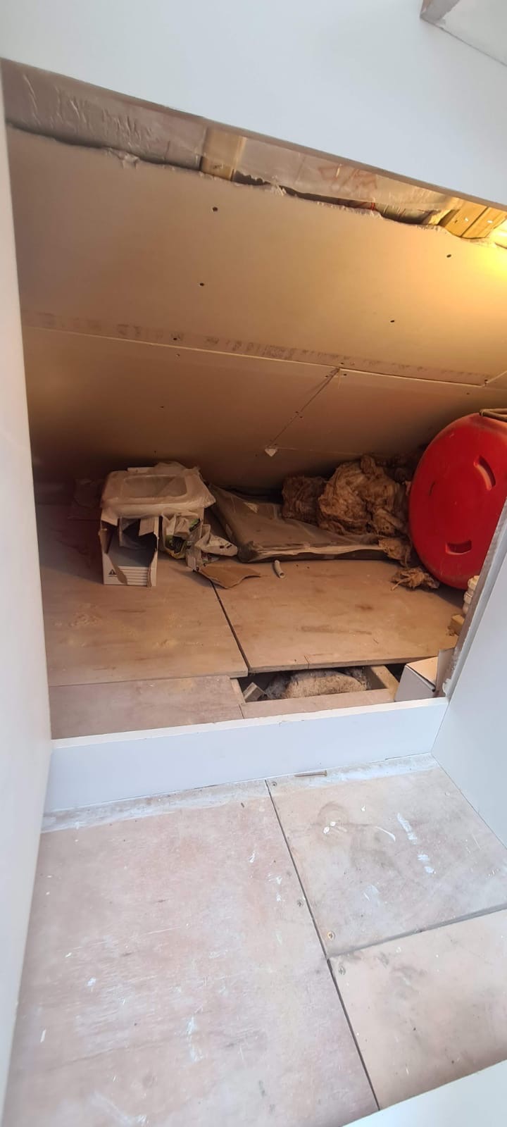 Poddasze w trakcie prac remontowych: widoczne płyty gipsowo-kartonowe na skosach, izolacja, nieużywana umywalka w opakowaniu, fragment podłogi z otworem, czerwony zbiornik.