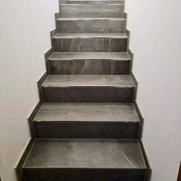 MAKS-FLIZ Uslugi Glazurnicze - Schody wyłożone szarymi płytkami imitującymi marmur, z widocznymi fugami i minimalistycznym wykończeniem przy ścianie.