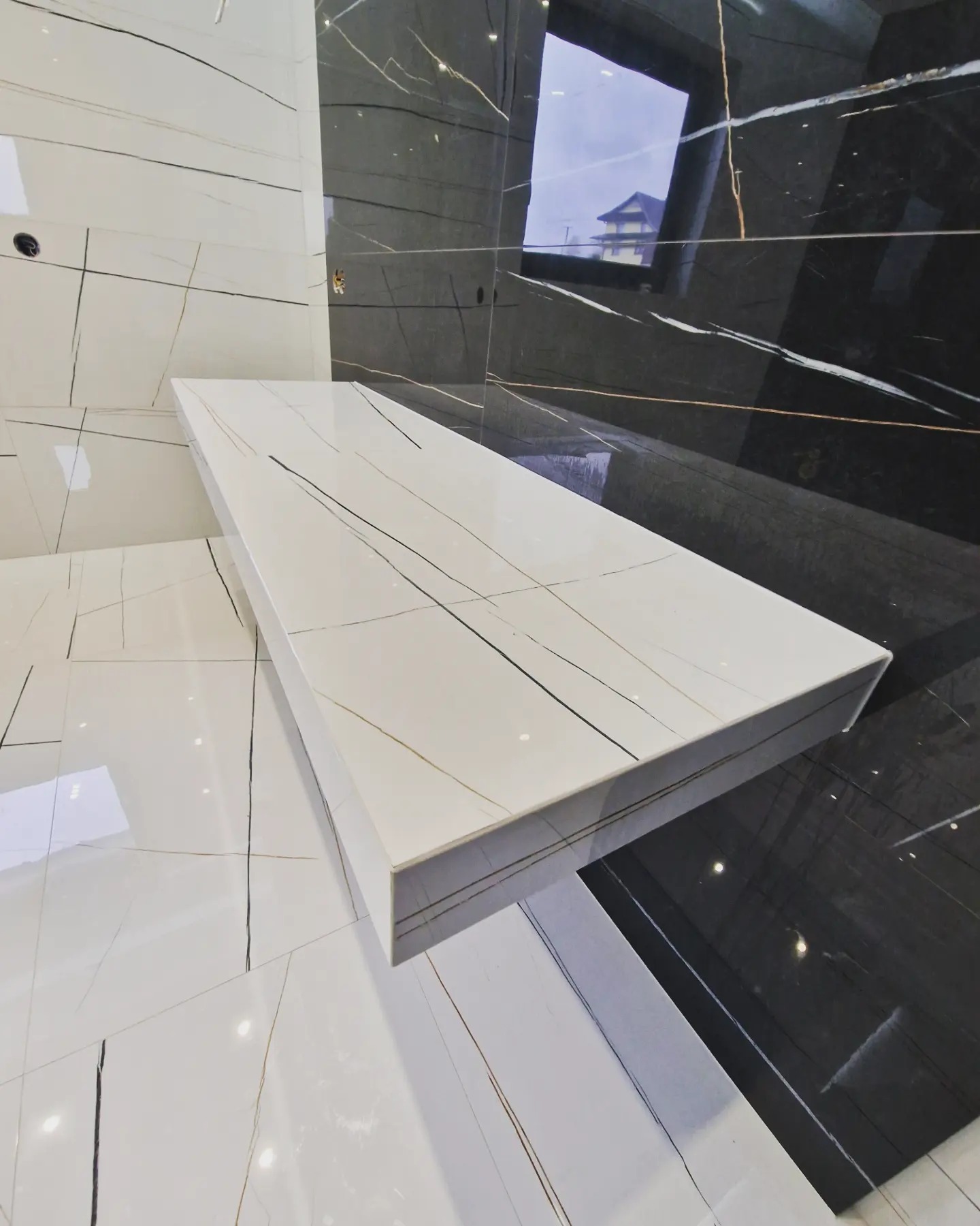 Nowoczesna łazienka z białymi i czarnymi płytkami imitującymi marmur, z półką z tego samego materiału, widok z góry.