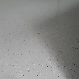 Jasnoszara podłoga z drobnymi, czarnymi i białymi elementami dekoracyjnymi, wykończona na wysoki połysk, widoczne odbicie światła.