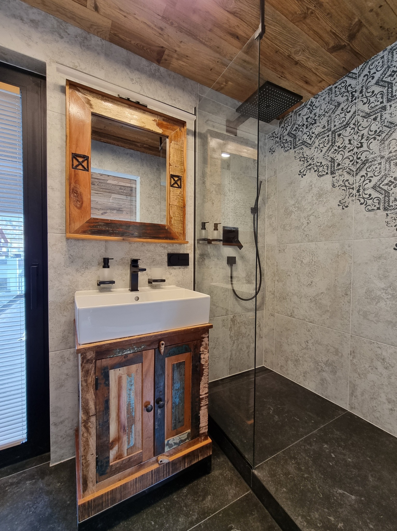Nowoczesna łazienka z kabiną typu walk-in, drewnianym sufitem i szafką pod umywalką z recyklingu drewna. Lustro w drewnianej ramie. Czarna armatura.