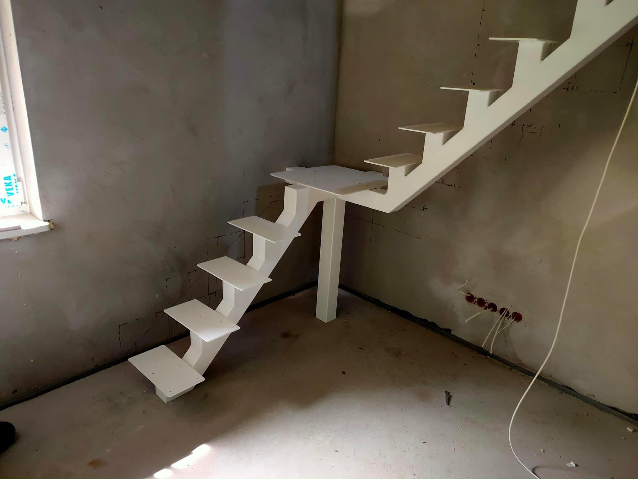 Białe, metalowe schody modułowe w surowym stanie, widoczne otwory na gniazdka elektryczne w ścianie, okno z profilem VEKA.