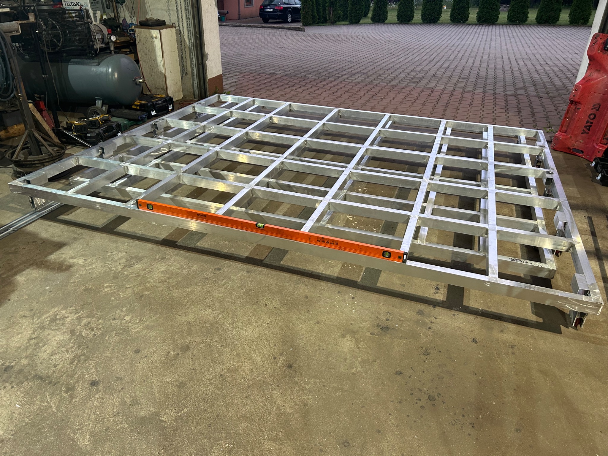 Metalowa konstrukcja kratowa z poziomnicą, na kółkach, w warsztacie.