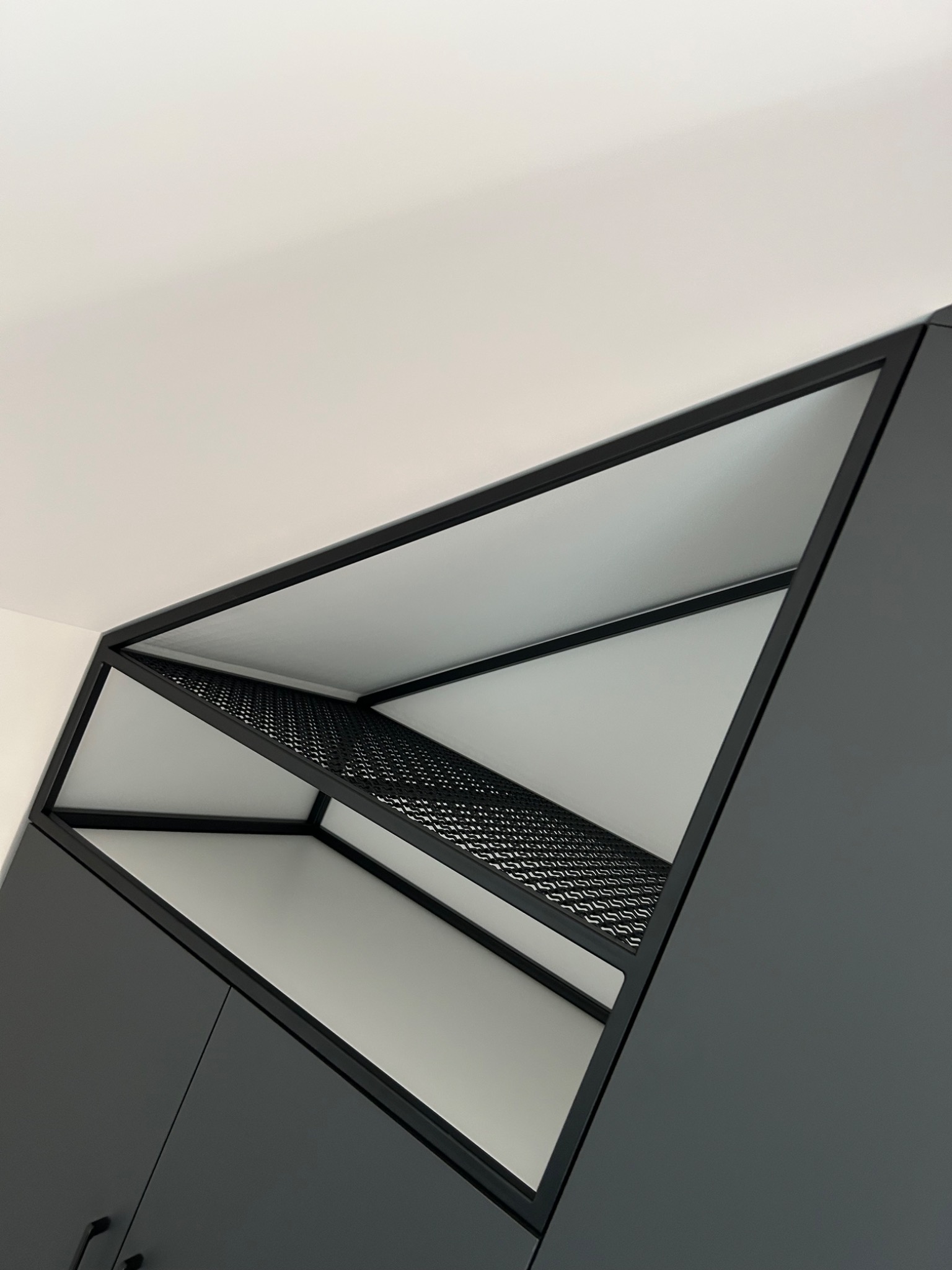 Nowoczesna, grafitowa szafa wnękowa z metalową, ażurową półką pod sufitem, widziana z dołu pod kątem.