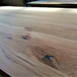 Jasny, surowy blat z litego drewna dębowego z widocznymi słojami, sękami wypełnionymi żywicą w kolorze granatowym i naturalnym wykończeniem.