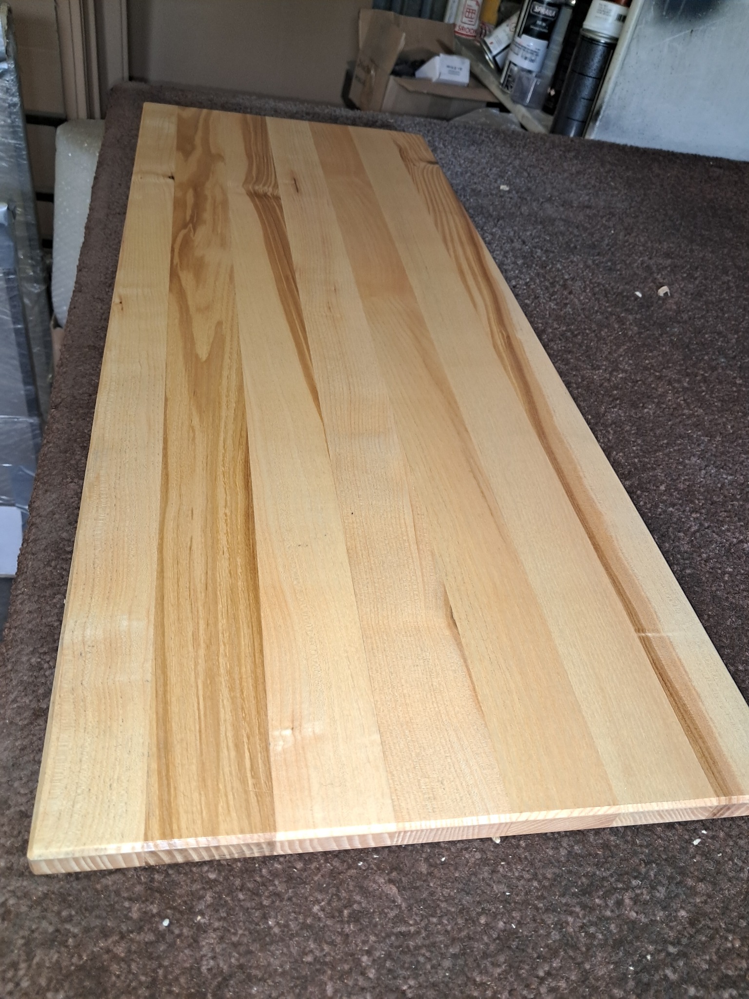 Surowy, prostokątny blat z jasnego drewna o wyraźnym usłojeniu, leżący na brązowym, teksturowanym podłożu w warsztacie.