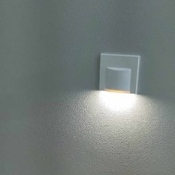 Fit-Bud Krzysztof Stasiak - Ściana z fakturą pomalowana na szaro, oświetlona przez nowoczesny kinkiet LED z ciepłym światłem.