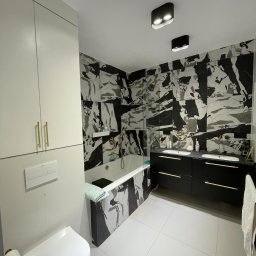 Małgorzata Kosek Zakład Produkcyjno-Usługowo-Handlowy Kosmebels - Nowoczesna łazienka z białą zabudową, toaletą podwieszaną, wanną i umywalkami na czarnej szafce z marmurowymi płytkami na ścianach.